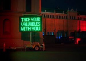 green neon sign saying Take Your Valuables With You, what is left is intatters