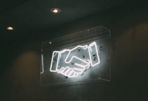 white neon sign of a handshake, nemesis, no handshakes due to covid